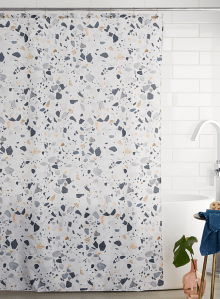 A cloth, terrazzo printed shower curtain is featured in a white bathroom.