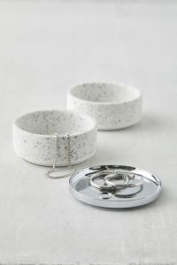 a pair of earring and a necklace are draped over an don two ceramic, terrazzo trinket boxes and its silver lid.